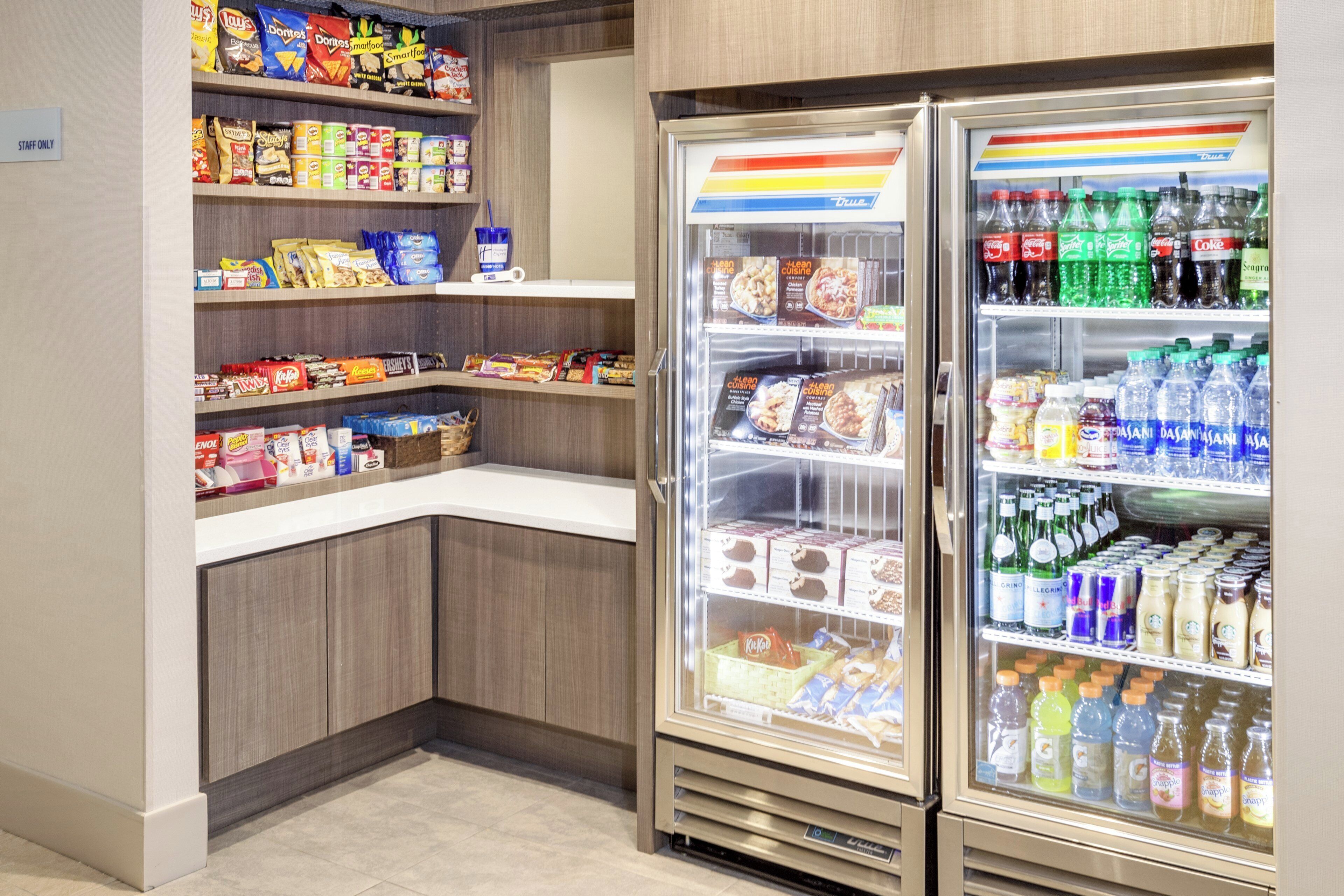 A self-service snack and beverage area with shelves stocked with various snacks and a refrigerated section with bottled water and juices.