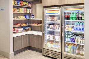 Un área autoservicio con aperitivos y bebidas, estantes llenos de diversos bocadillos y una sección refrigerada con agua embotellada y jugos.