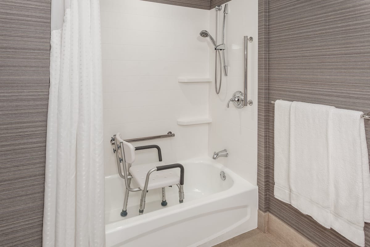 A modern bathroom with a white bathtub, grab bars, a showerhead, and a towel rack.
