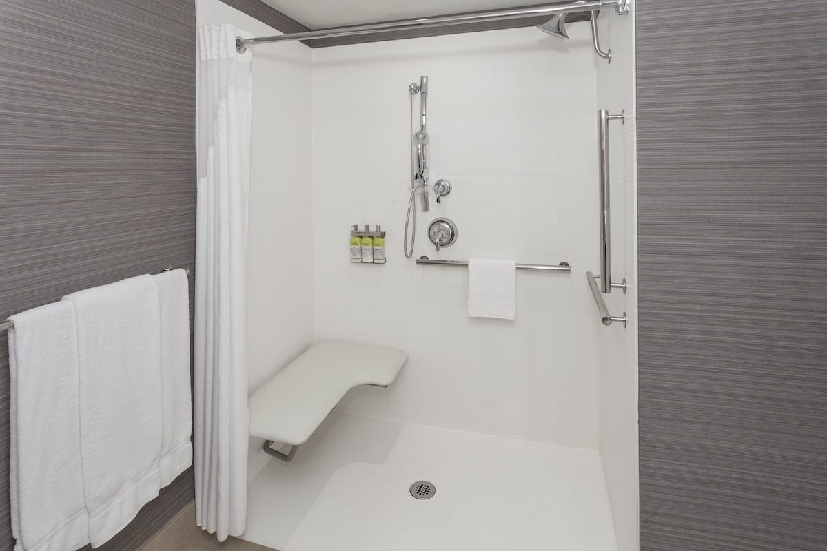 A walk-in shower with a grab bar, a white towel, and a showerhead.