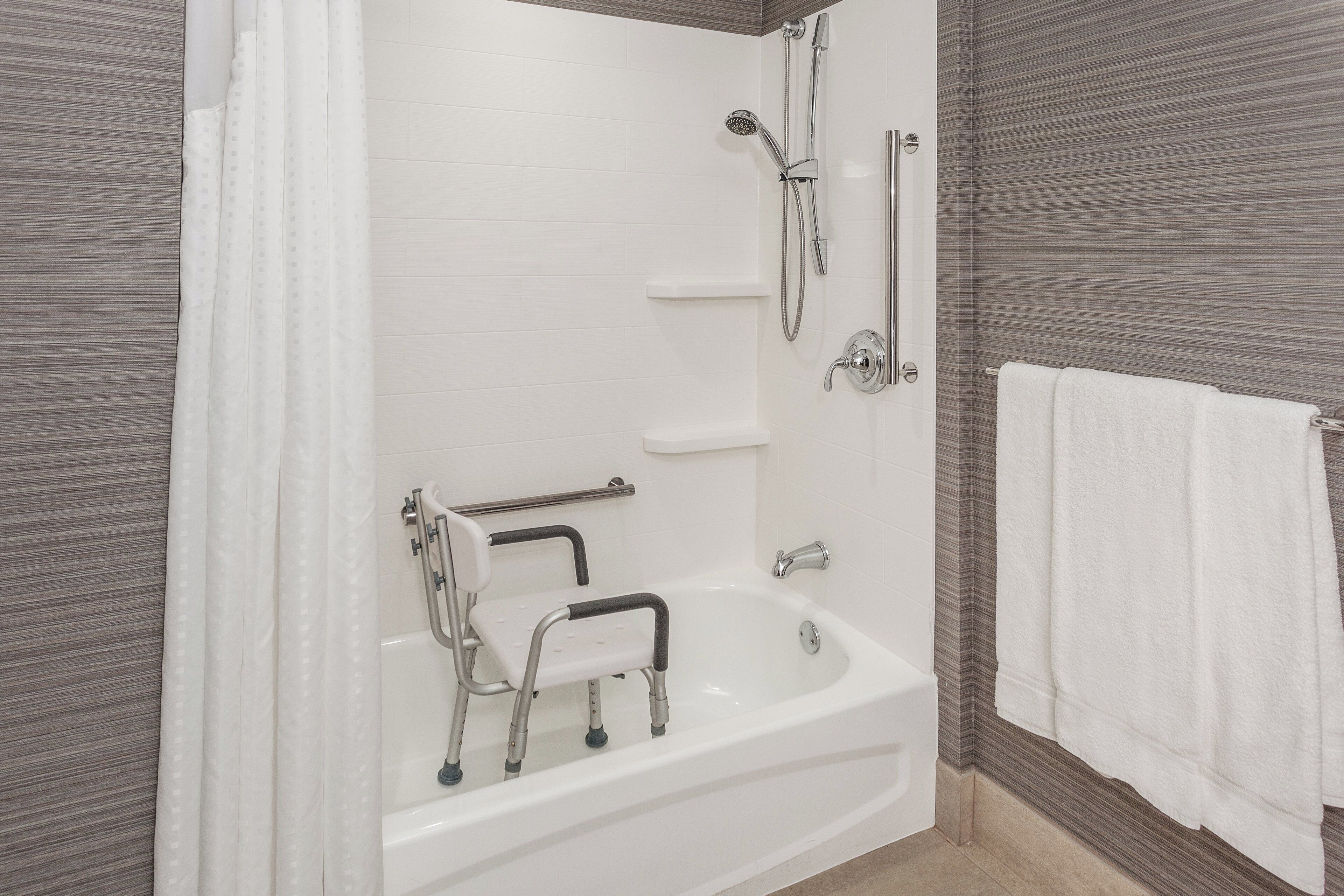A bathroom with a white bathtub, a shower, and a grab bar.