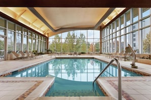 Una piscina interior con paredes de vidrio transparente, sillones de descanso y un solárium con baldosas.