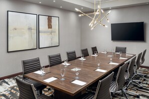 Une salle de conférence avec une longue table, des chaises, un téléviseur à écran plat et des œuvres d’art abstrait accrochées au mur.