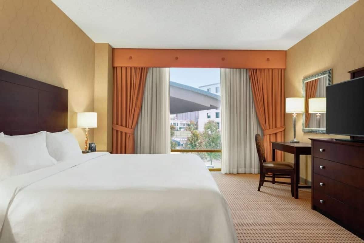 Une chambre d’hôtel équipée d’un lit, d’un bureau, d’une chaise, d’une télévision et d’une fenêtre avec des rideaux.
