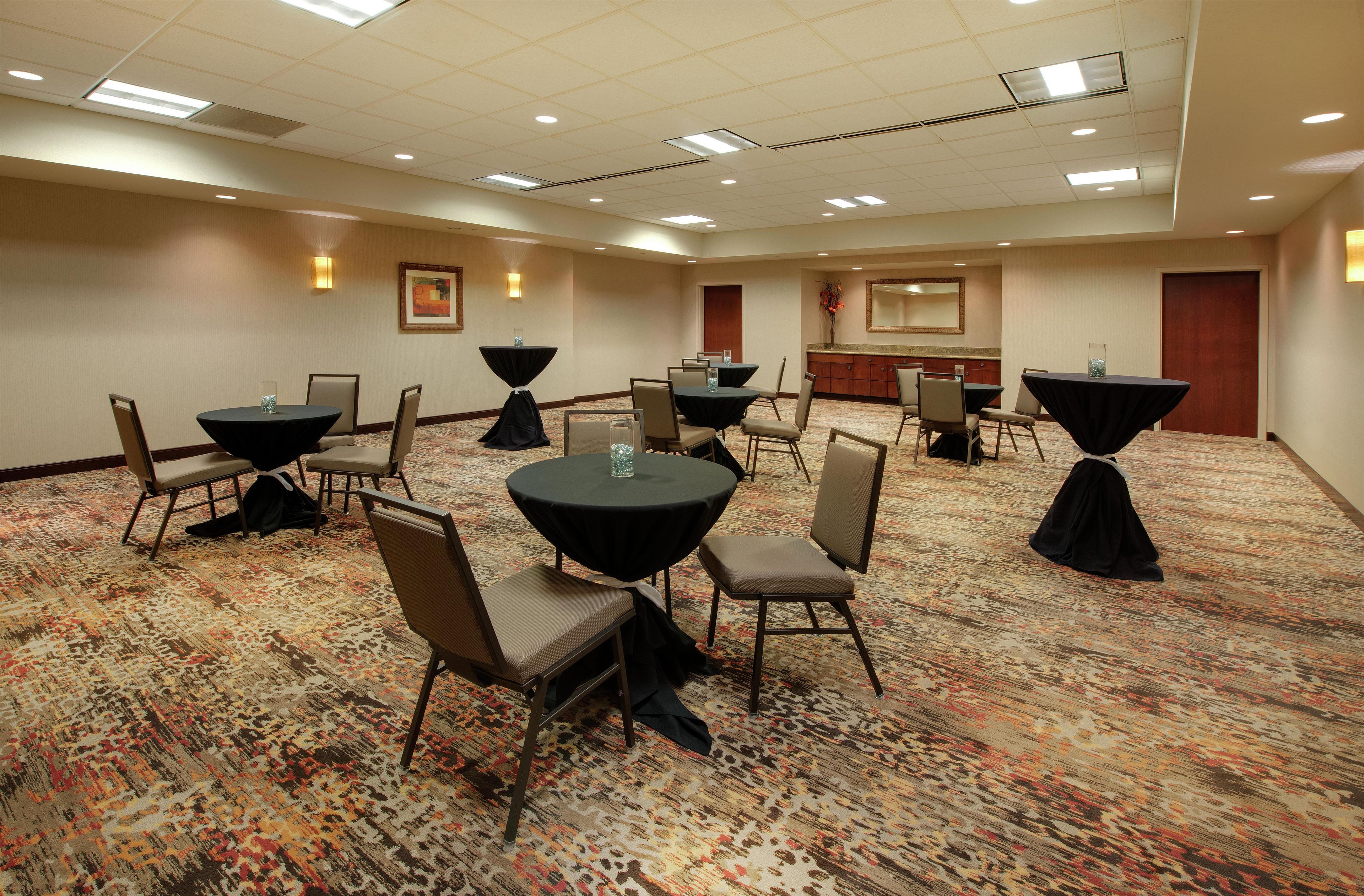 A conference room with multiple tables and chairs, carpeted flooring, and ceiling lights.