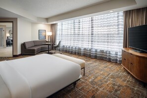 Une chambre d’hôtel avec un grand lit, un bureau, une chaise, une télévision et une moquette à motifs.