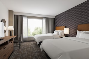 Ein Hotelzimmer mit zwei Betten, einem Schreibtisch, einem Stuhl, einem Fernseher und einem Fenster mit Vorhängen.
