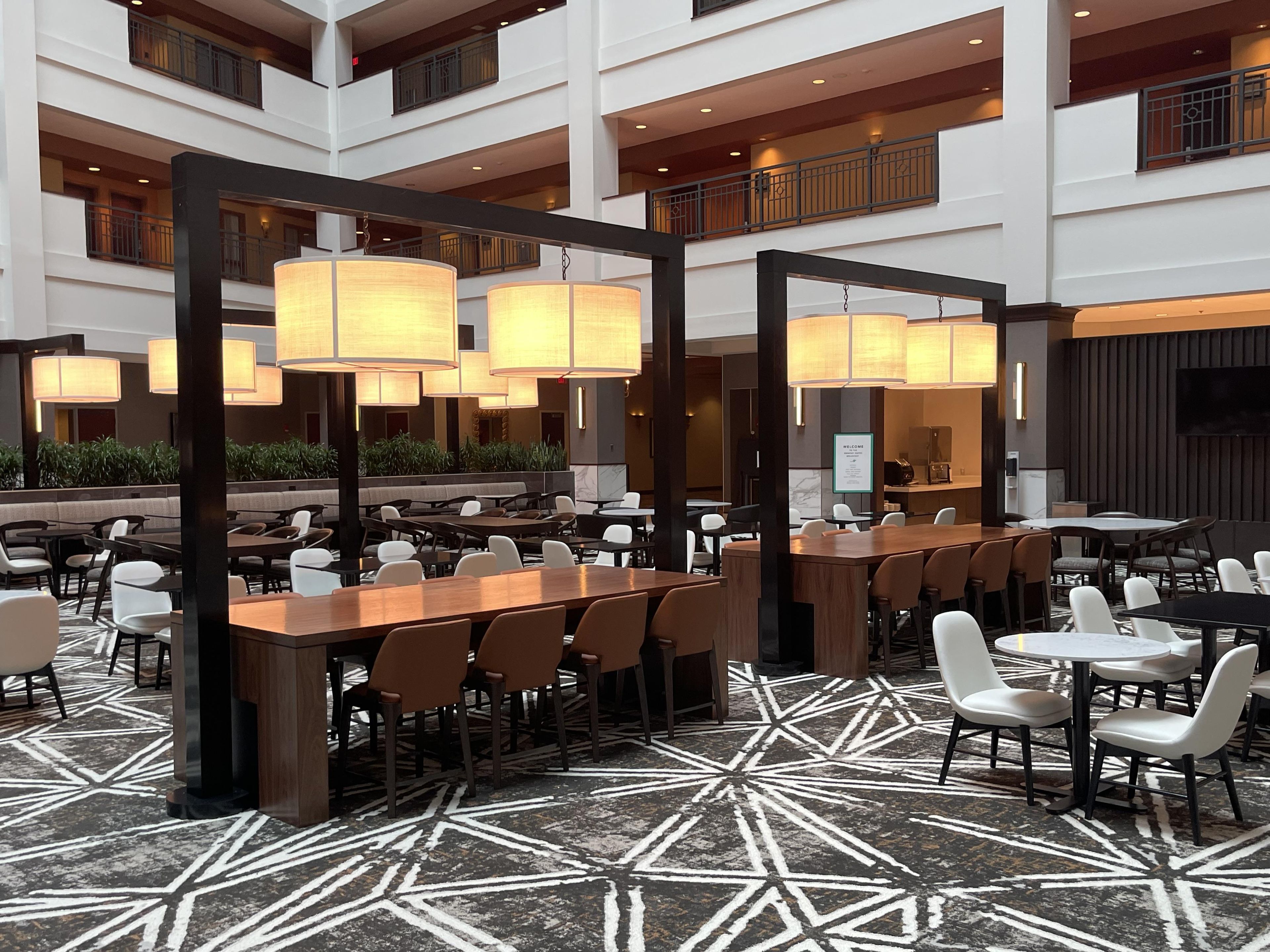 A hotel lobby with multiple dining areas, large chandeliers, and a patterned floor.