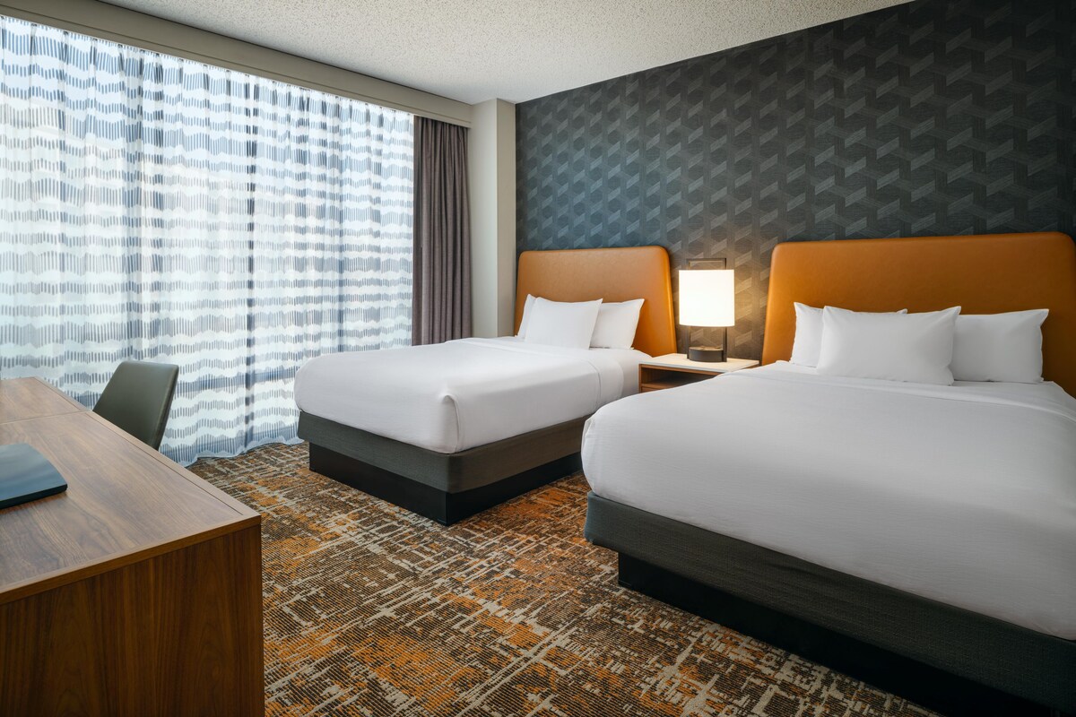 Ein Hotelzimmer mit zwei Betten, einem Schreibtisch und einem gemusterten Teppich.