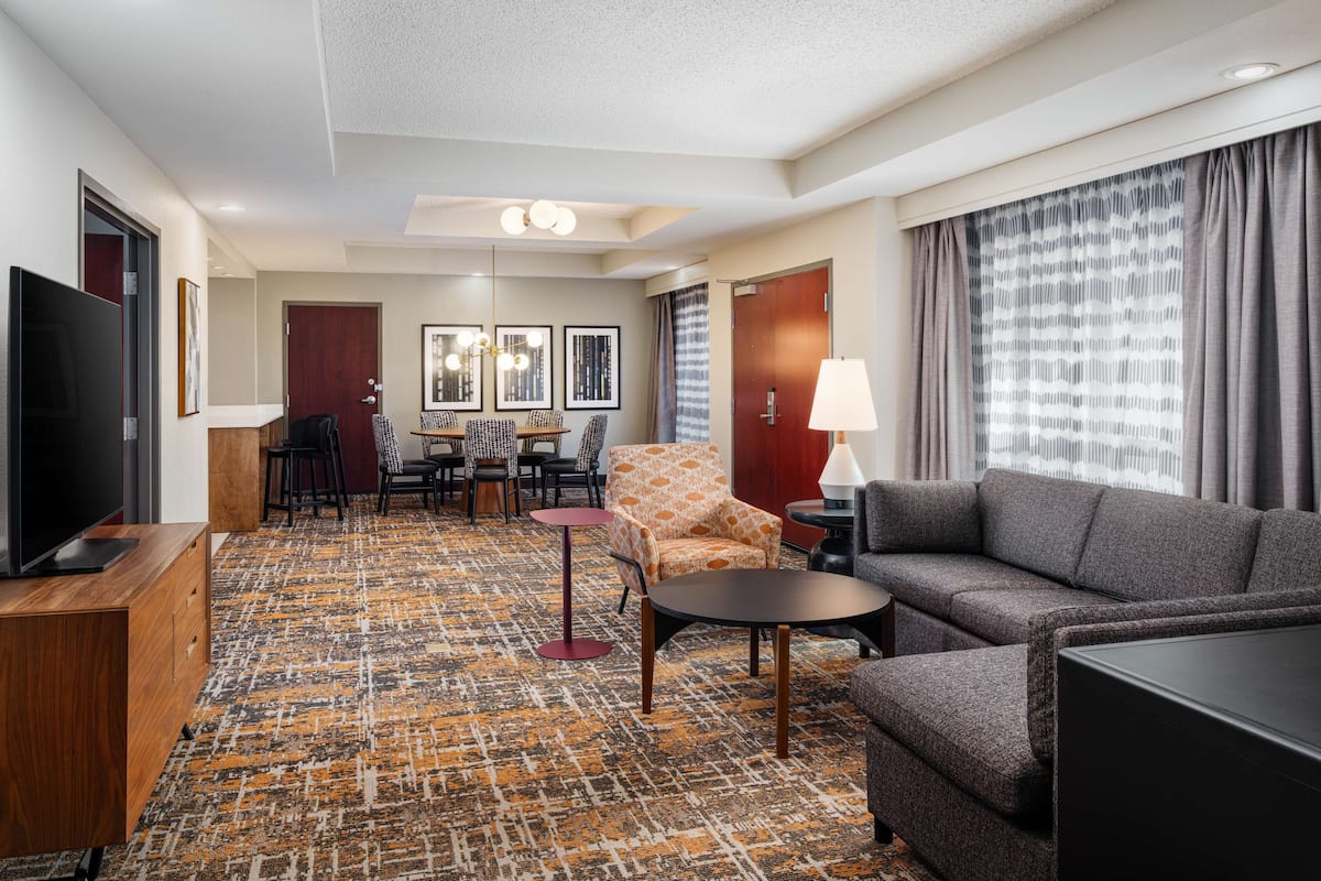 Une chambre d’hôtel dotée d’un grand téléviseur à écran plat, d’un canapé, d’un coin repas avec des chaises et une table, ainsi que d’une moquette à motifs.