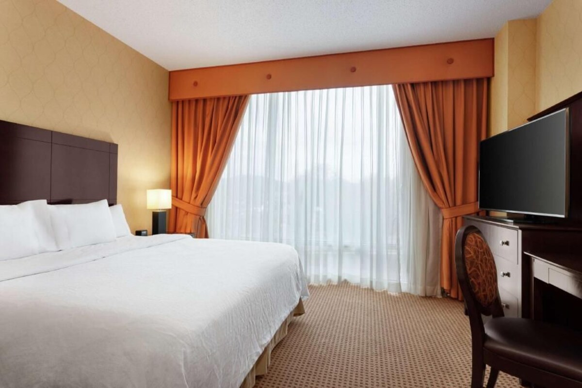 A hotel room with a large bed, a TV, a desk, and a window with curtains.