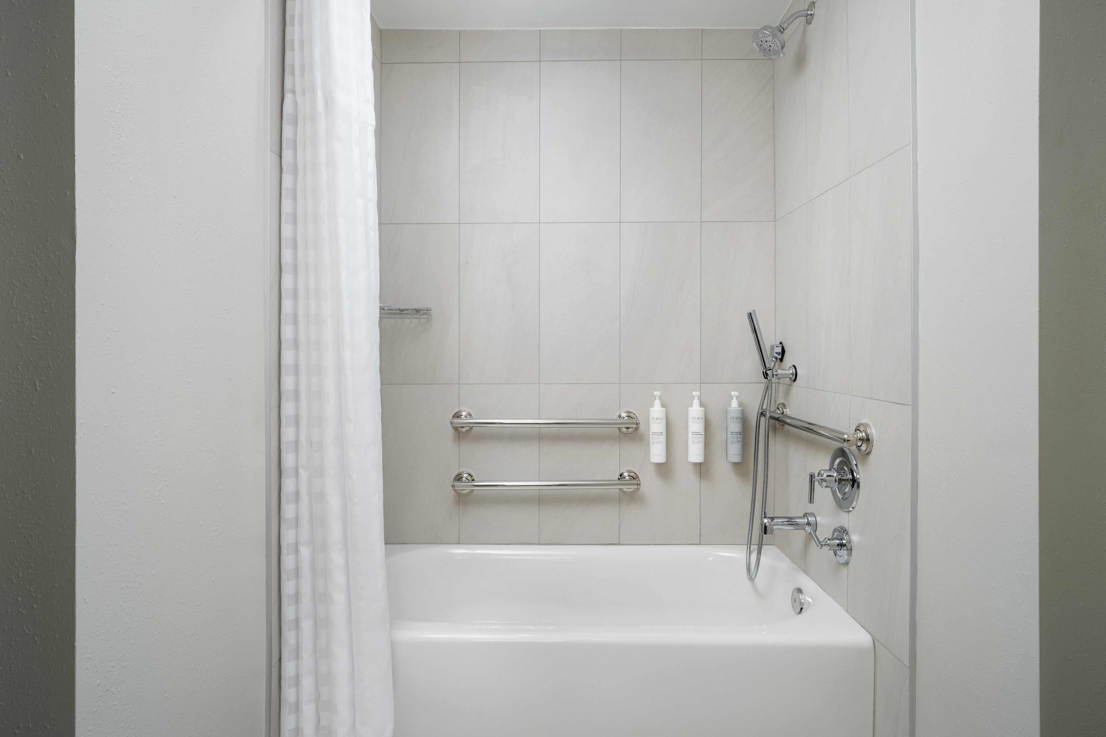 A modern bathroom with a bathtub, grab bars, and toiletries.