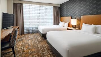 A hotel room with two beds, a desk, a TV, and a patterned carpet.