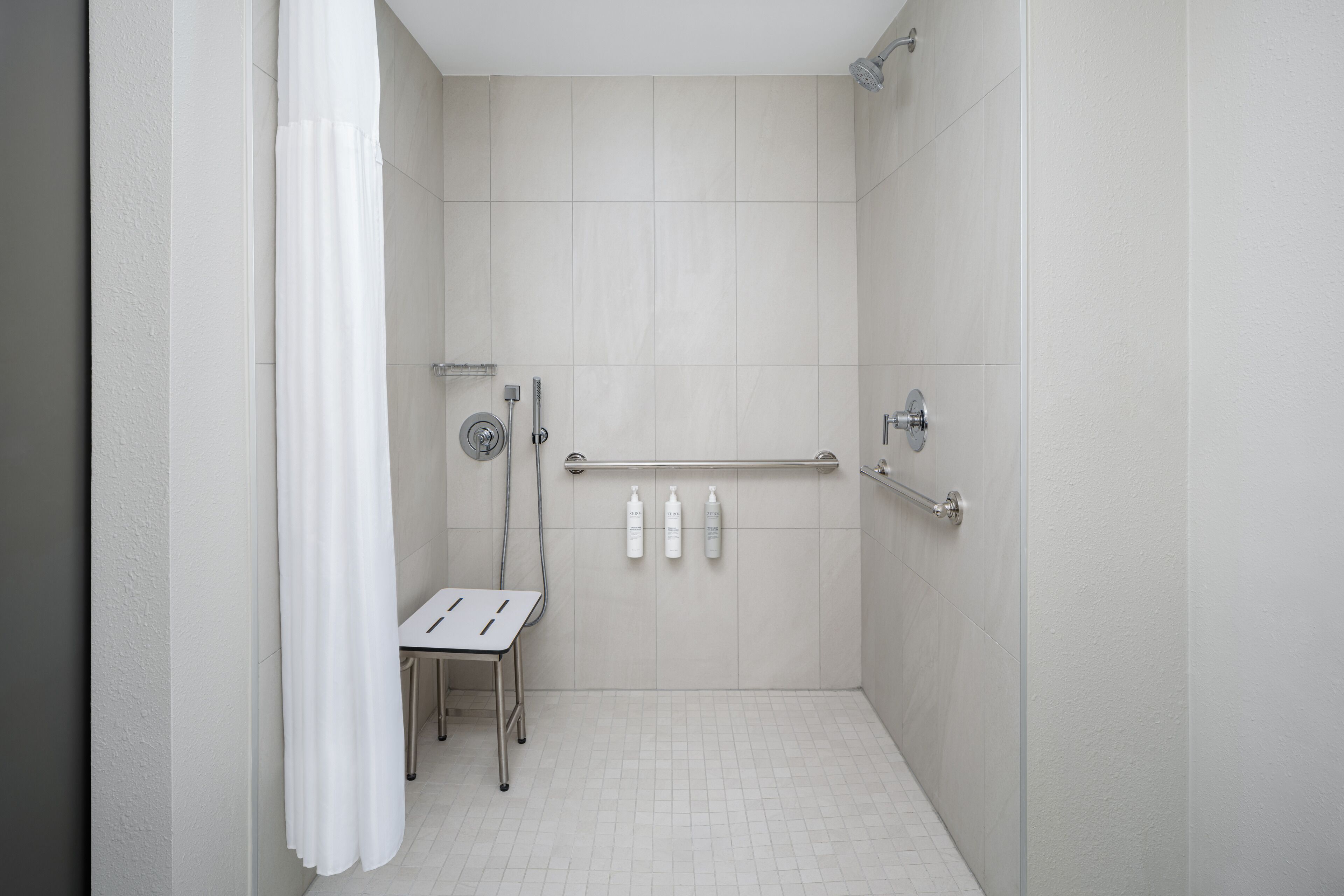 Een moderne badkamer met een douche, handgrepen en een klein tafeltje met toiletartikelen.