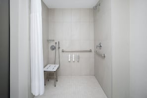 Een moderne badkamer met een douche, handgrepen en een klein tafeltje met toiletartikelen.