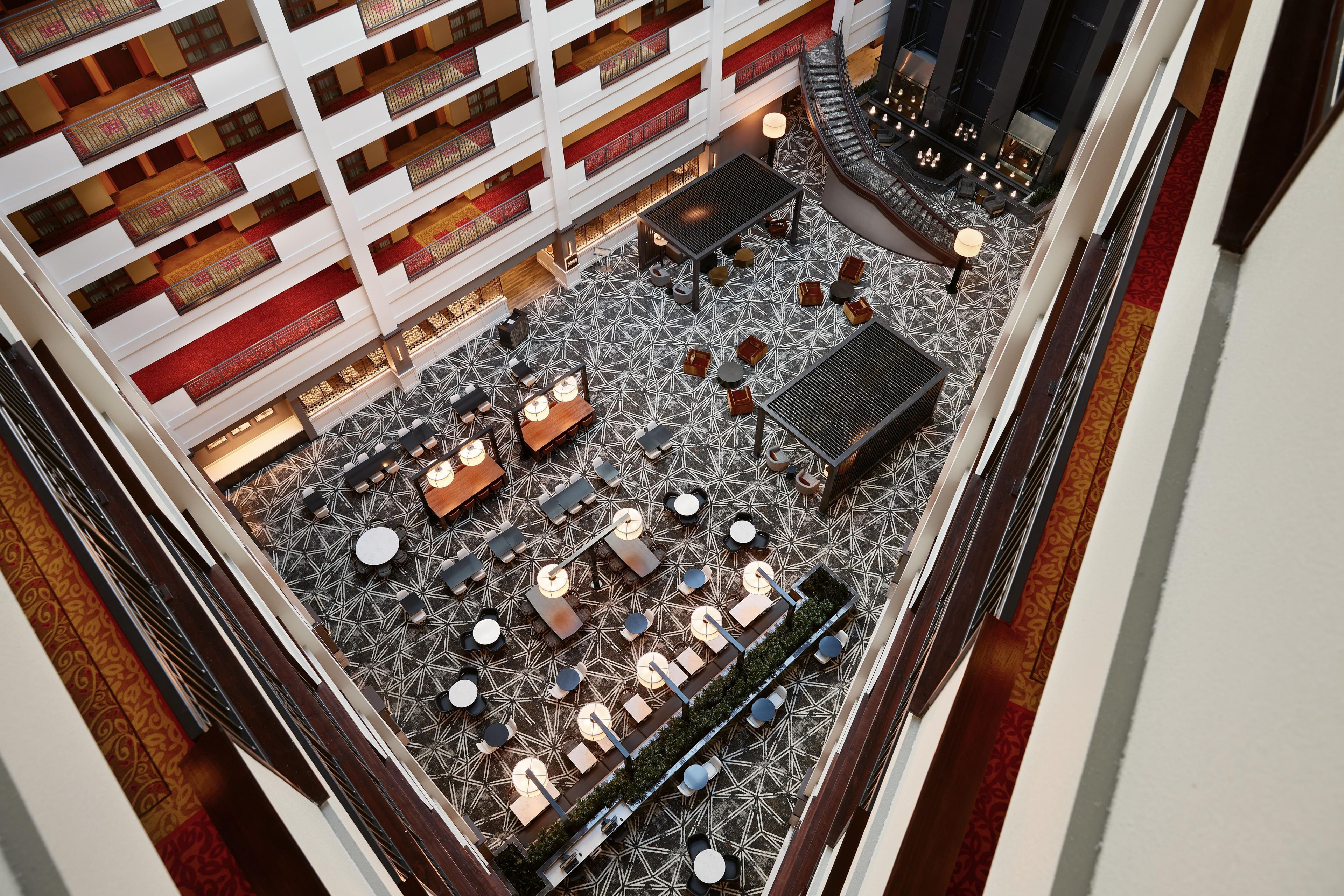An indoor atrium with multiple levels of balconies, a central open space with tables and chairs, and a patterned floor.