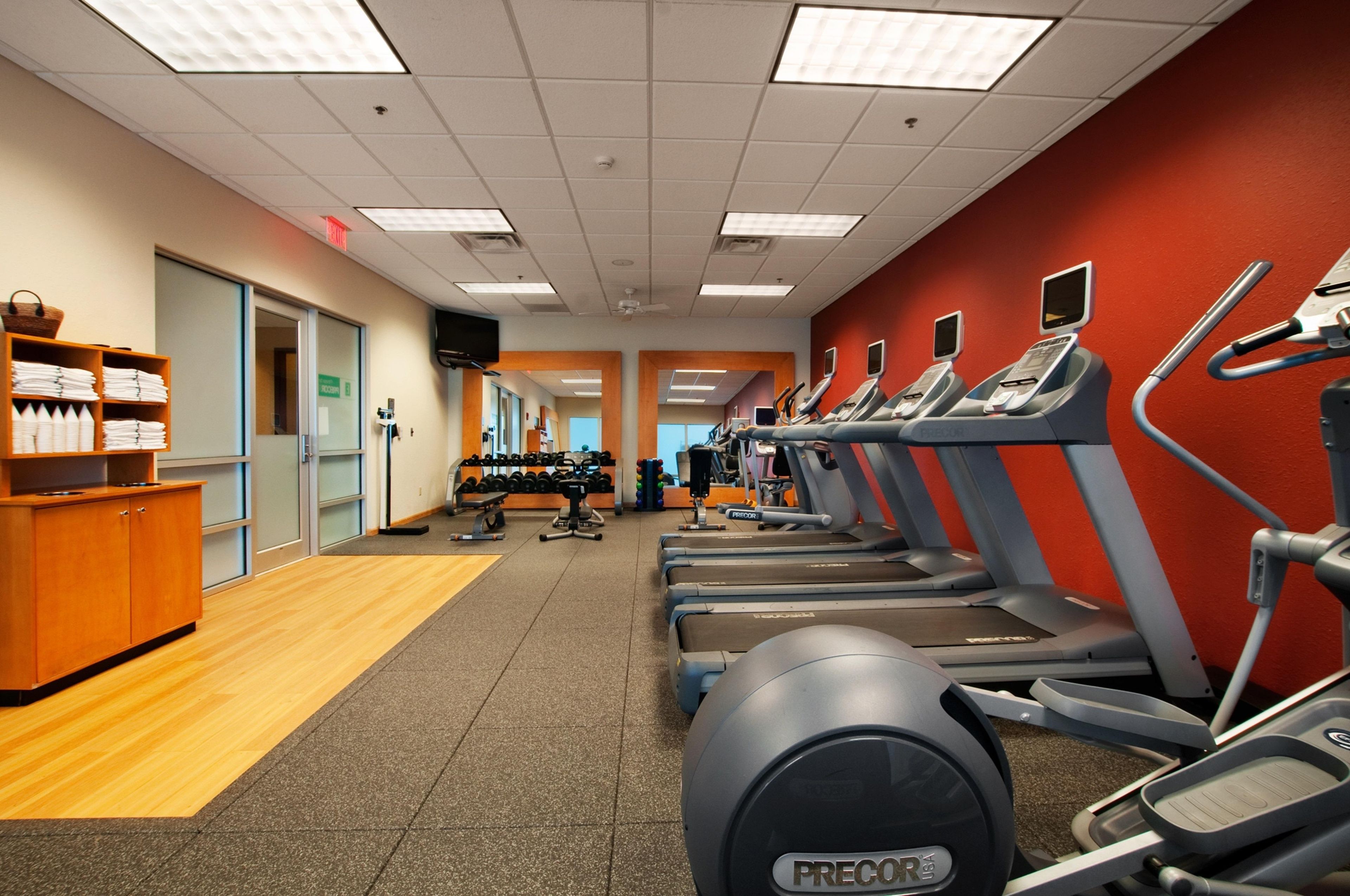 A gym with treadmills, weights, and a wooden cabinet with towels.