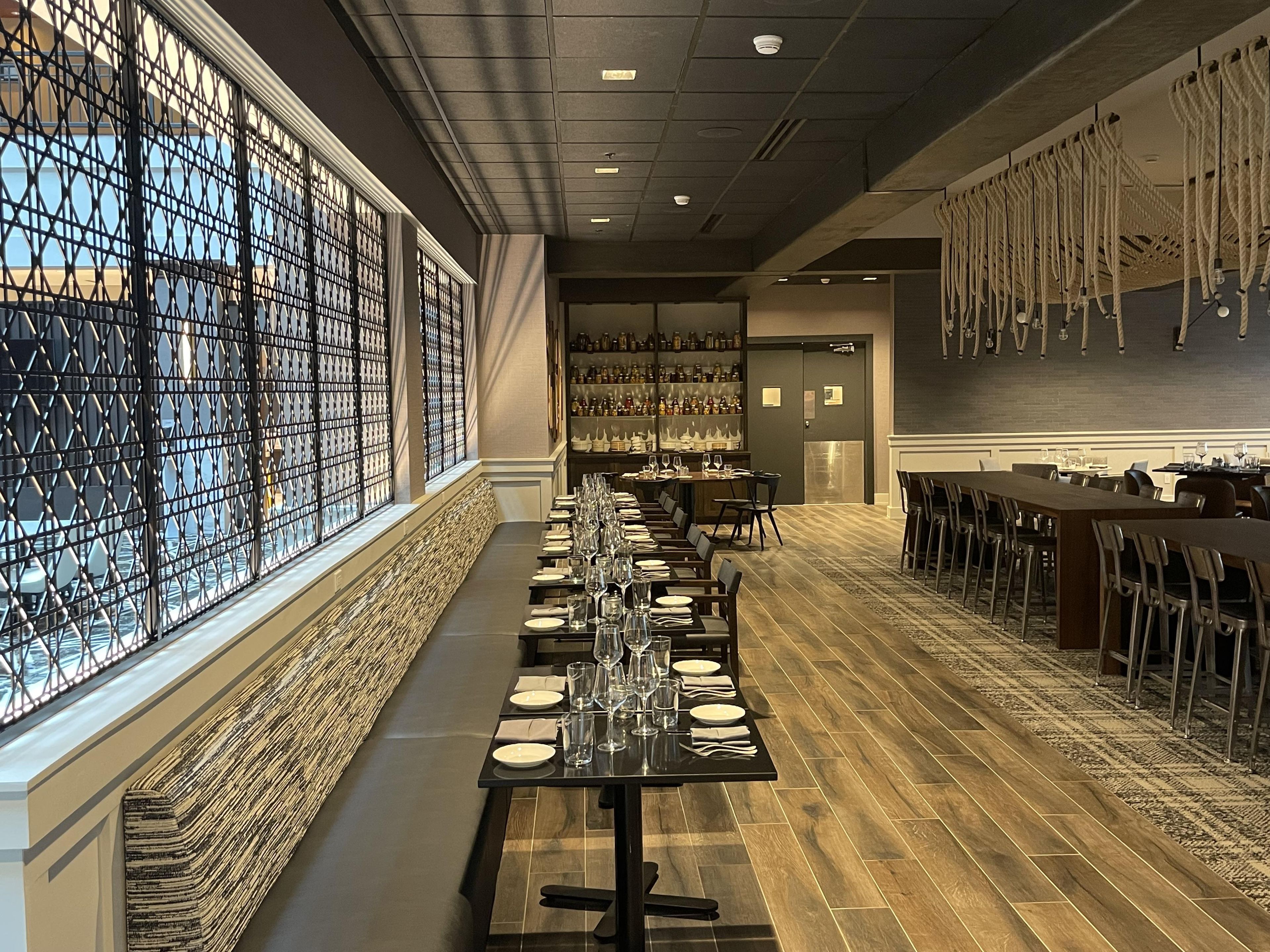 A long dining table set with chairs, a bar area with bottles, and a patterned wall.