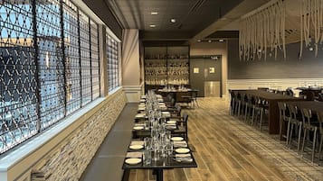 A long dining table set with chairs, a bar area with bottles, and a patterned wall.
