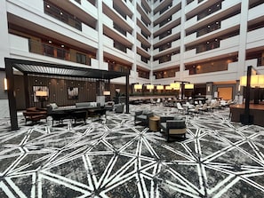Un hall d’hôtel à plusieurs niveaux, doté d’un sol aux motifs géométriques, d’espaces de détente et d’un design moderne.