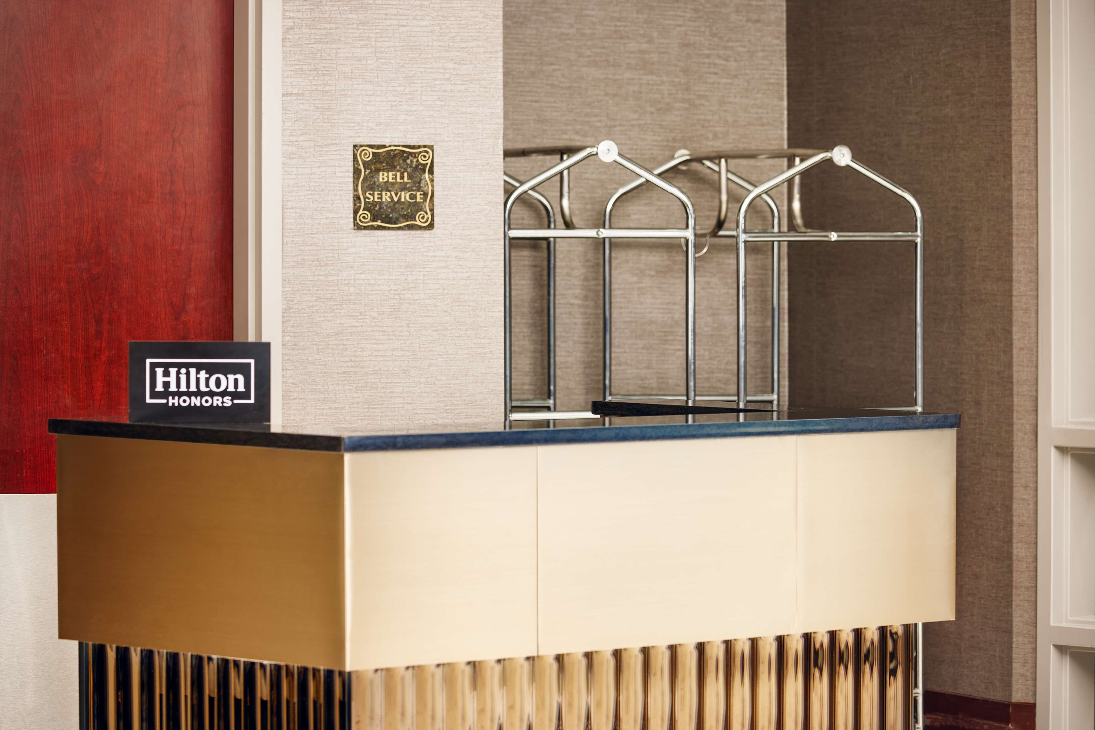 A hotel reception desk with a sign reading "Hilton Honors" and a "Bell Service" sign above it.