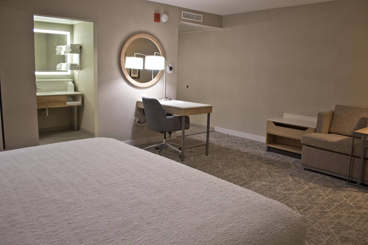 A hotel room with a bed, a desk with a chair, a round mirror, a small round table, and a sofa.
