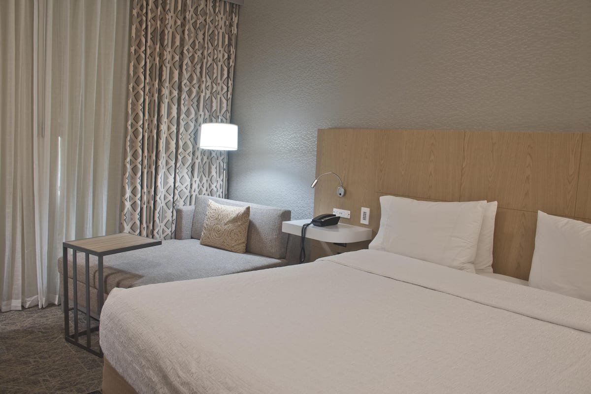 A hotel room with two beds, a bedside table with a lamp, a phone, and a patterned curtain.