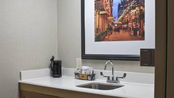Un baño de hotel pequeño con un lavabo, un espejo y un cuadro enmarcado con una vista urbana.