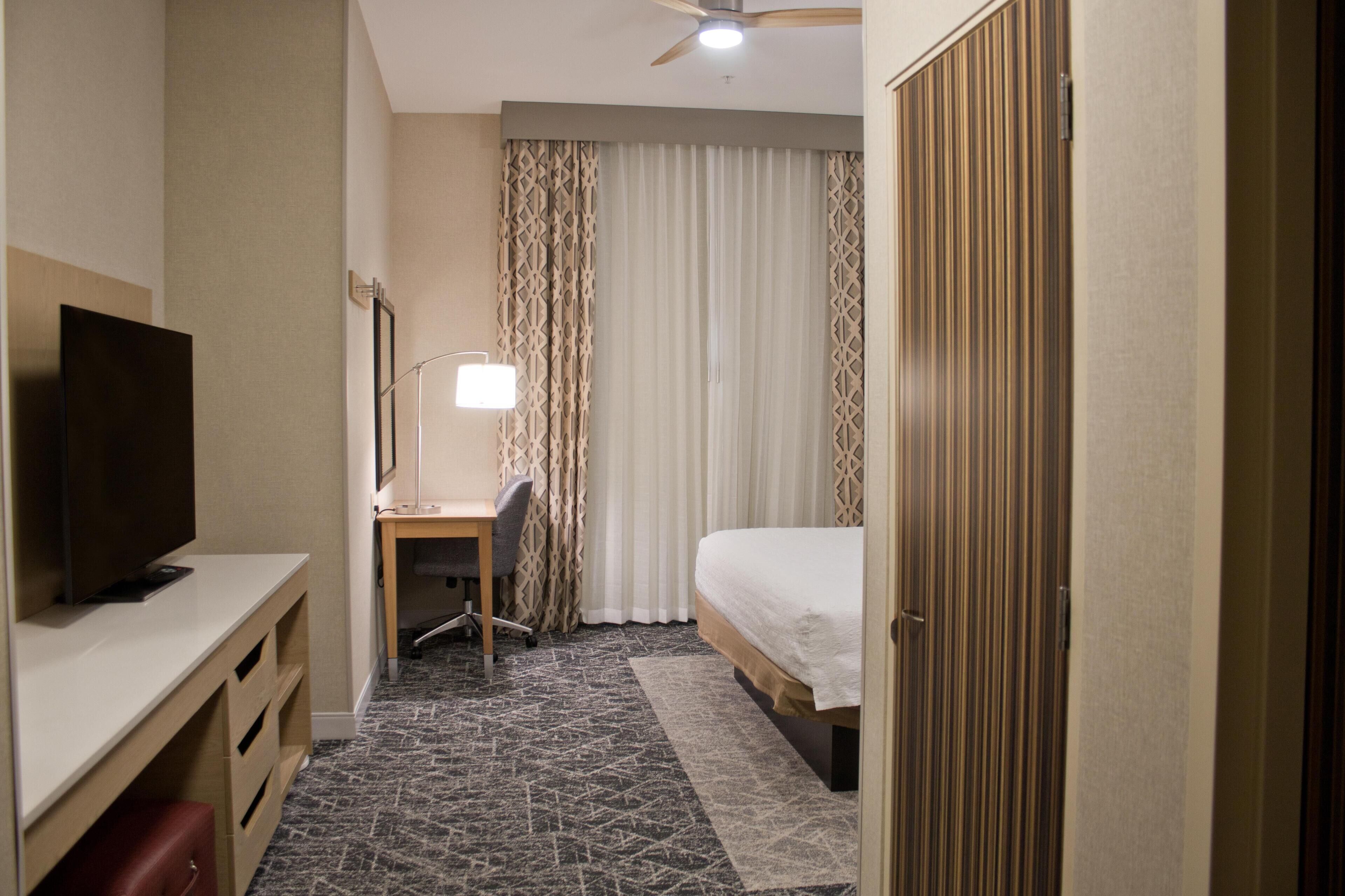 A hotel room with a bed, desk, TV, and a ceiling fan.