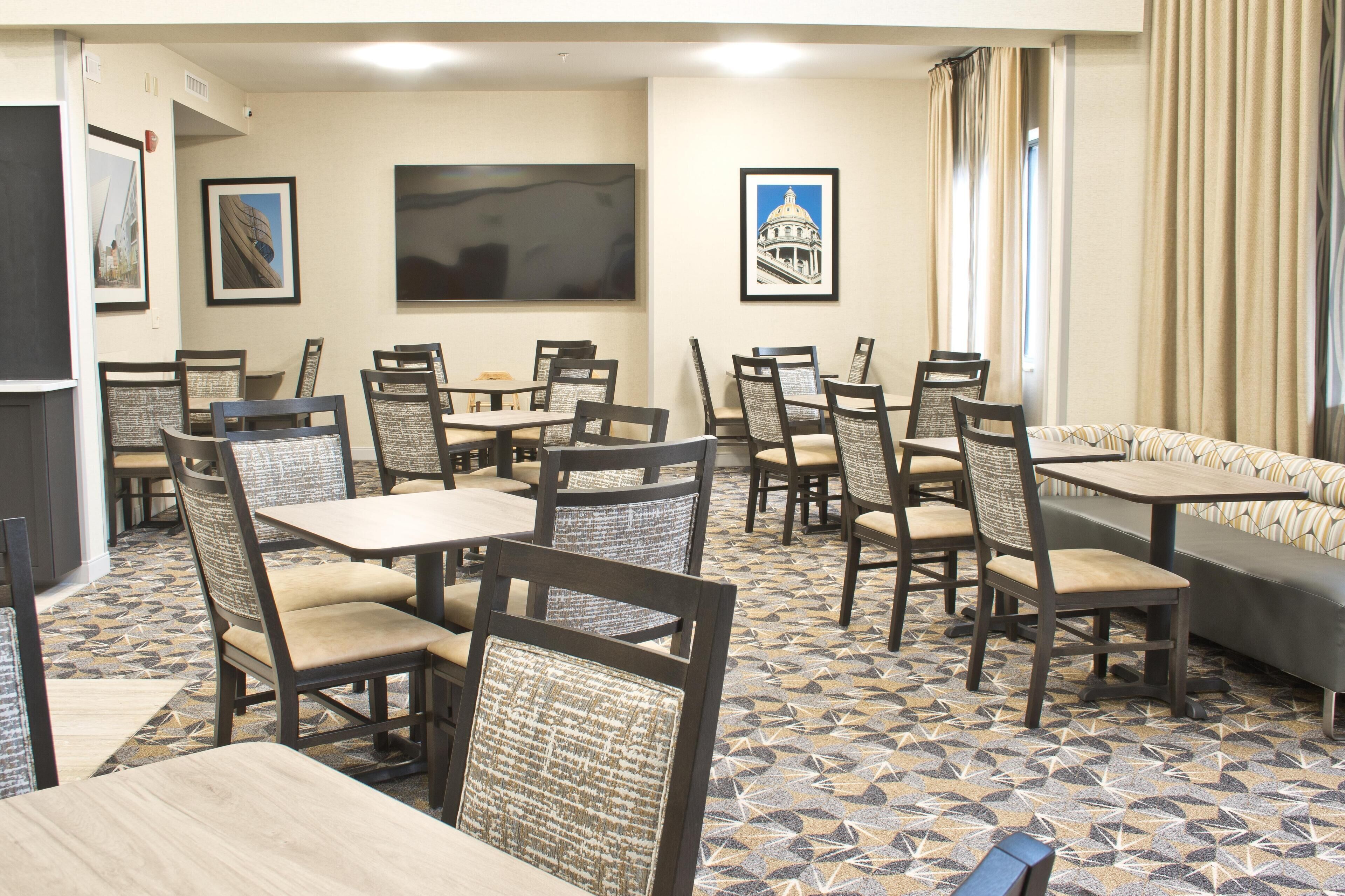 Een restaurantgedeelte in een hotel, met meerdere tafels en stoelen, kunstwerken aan de muren en een vloer met een patroon.