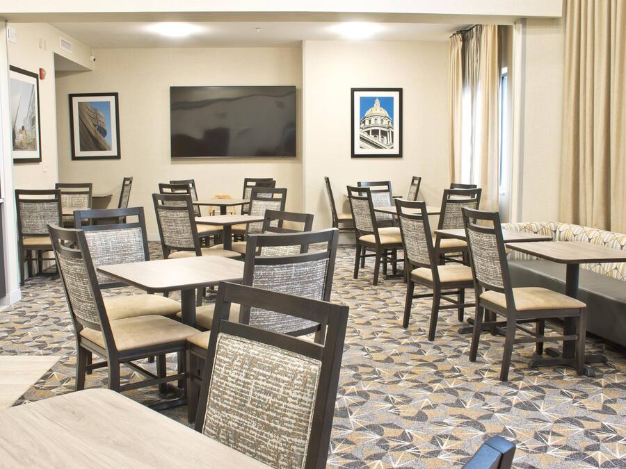 Een restaurantgedeelte in een hotel, met meerdere tafels en stoelen, kunstwerken aan de muren en een vloer met een patroon.
