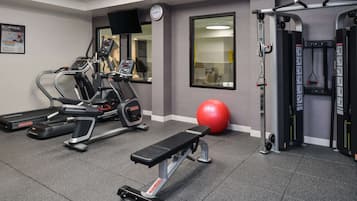 Un gimnasio con máquinas de cardio, una banca, una pelota de ejercicio roja y equipo de levantamiento de pesas.