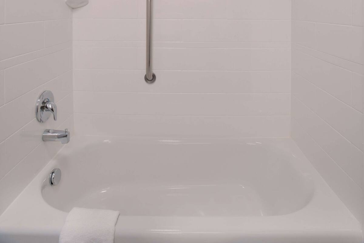 A modern bathroom with a bathtub, a handrail, and a faucet.