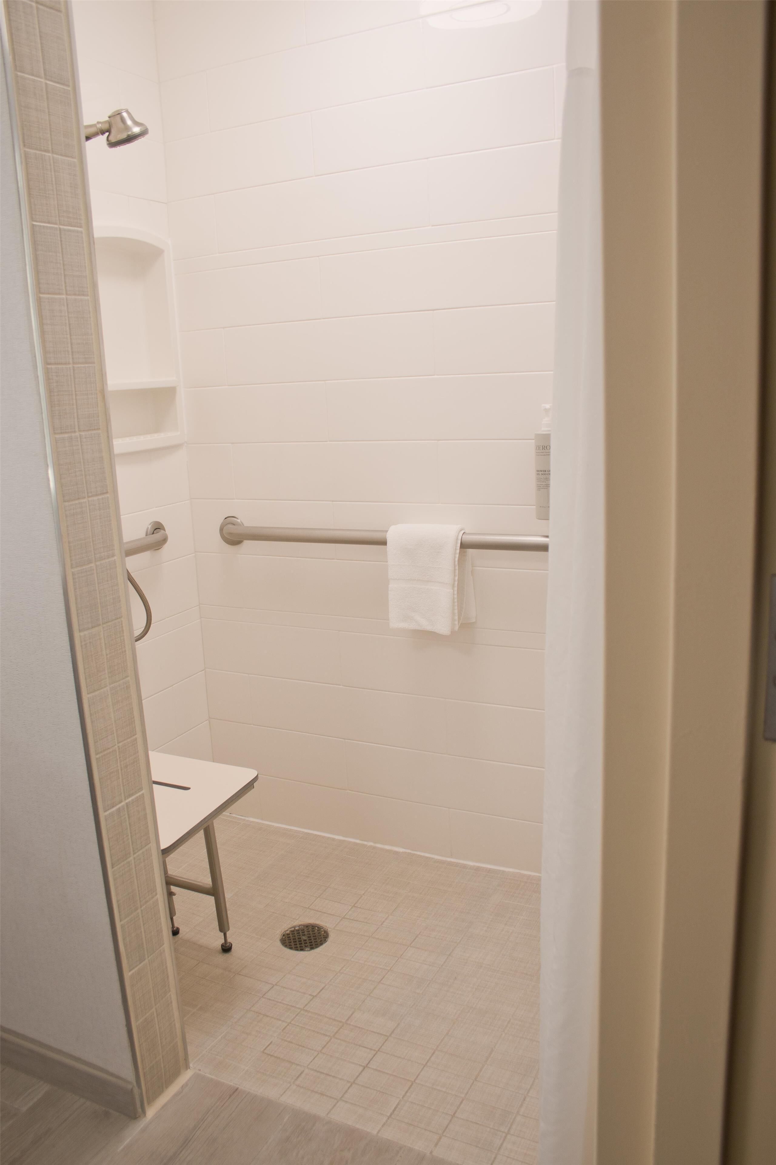 A bathroom with white tiled walls, a white toilet, a grab bar, and a towel hanging on the grab bar.