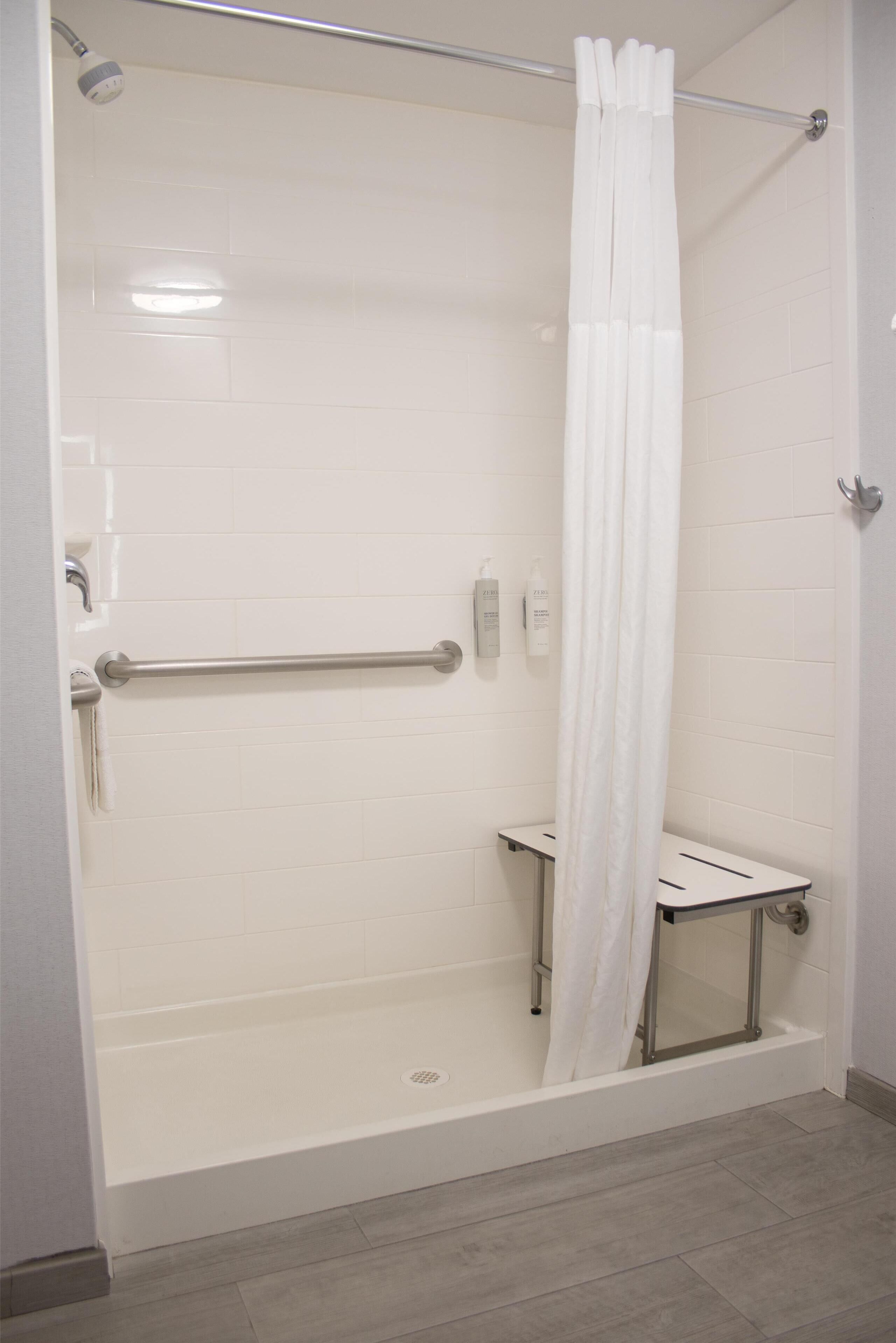 Eine barrierefreie Dusche mit weißem Duschvorhang, einer Haltestange und einer Handbrause.