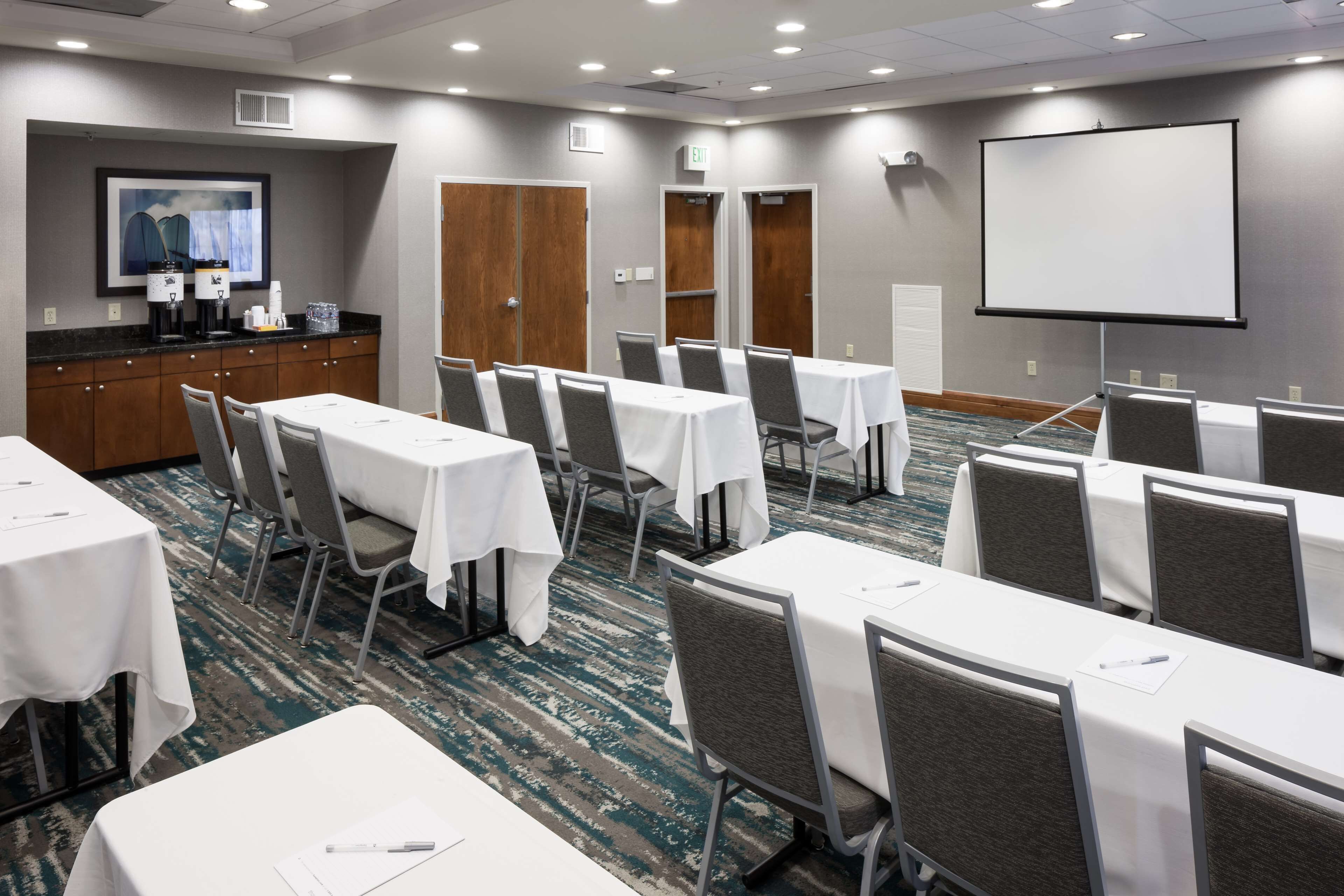 A conference room with tables, chairs, a projector screen, and a coffee station.