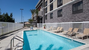 A swimming pool with lounge chairs and a white fence. - Hampton Inn Los Angeles-Orange County-Cypress (Cypress)
