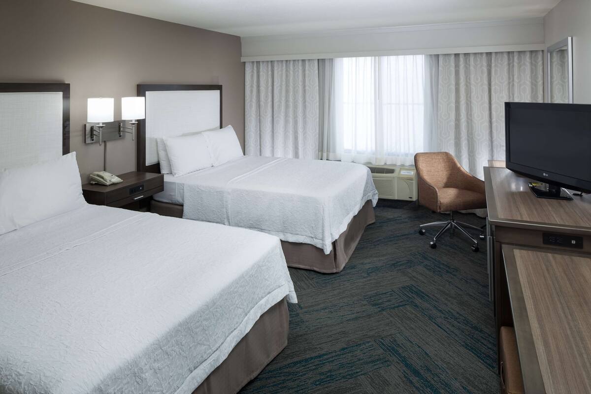 A hotel room with two beds, a TV, a desk, and a chair.