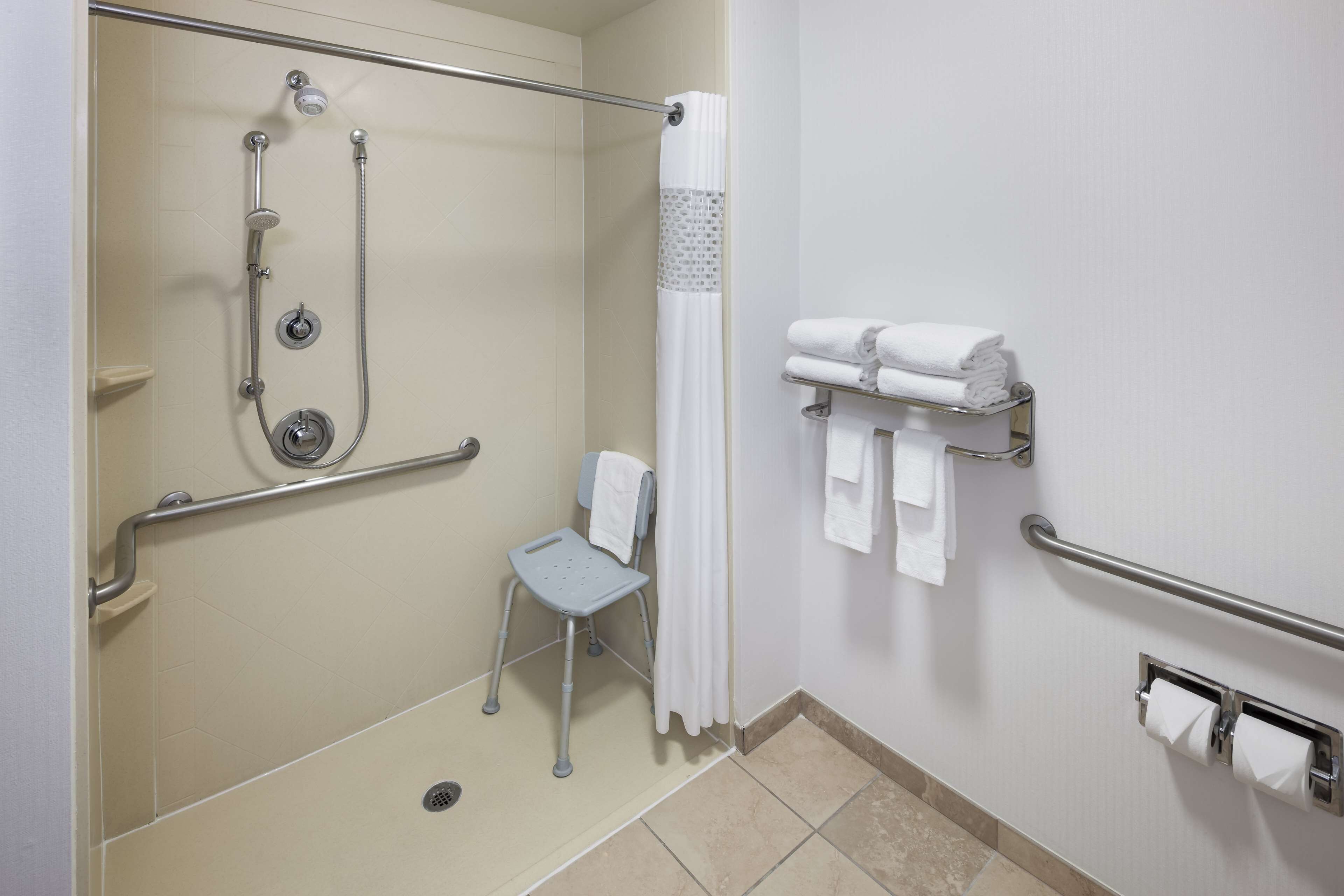 A shower with a grab bar, a chair, and a towel rack with towels.
