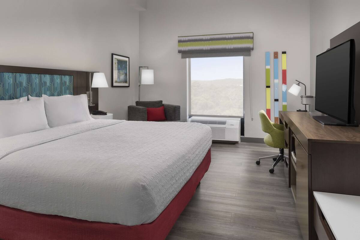 A hotel room with a large bed, a desk with a computer, a chair, and a TV.