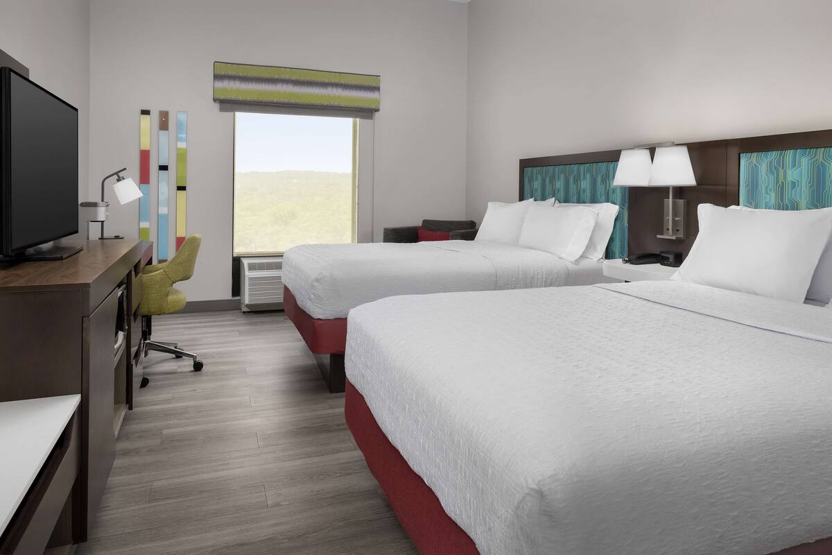 A hotel room with two beds, a desk with a computer, a chair, and a TV.