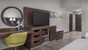 Een hotelkamer met een houten bureau, een flatscreen-televisie, een gele bureaustoel, een bed en een grote spiegel.