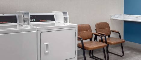 A laundry area with two washing machines and two chairs.