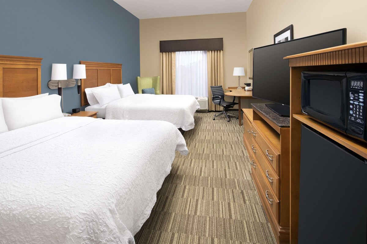 A hotel room with two beds, a desk, a television, and a minibar.