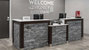 Een receptiebalie met een bord waarop staat 'WELCOME TO THE HONEY BEE STATE', een Hilton Honors logo en een digitale kiosk.