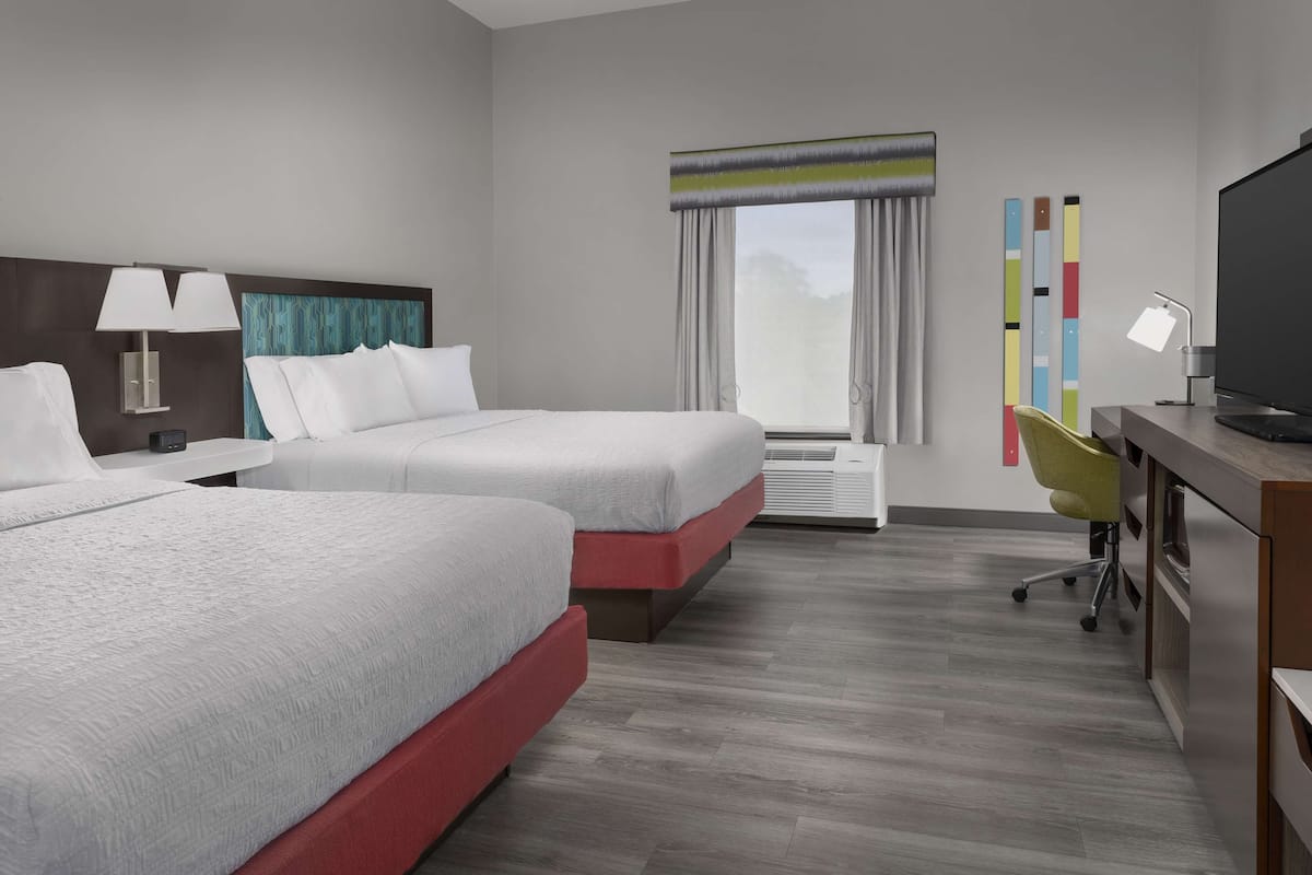 A hotel room with two beds, a desk, a chair, a TV, and a window with curtains.
