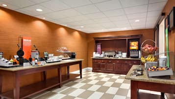 Vestíbulo de hotel con suelo a cuadros, una larga recepción, una estación de café y una exhibición de frutas.