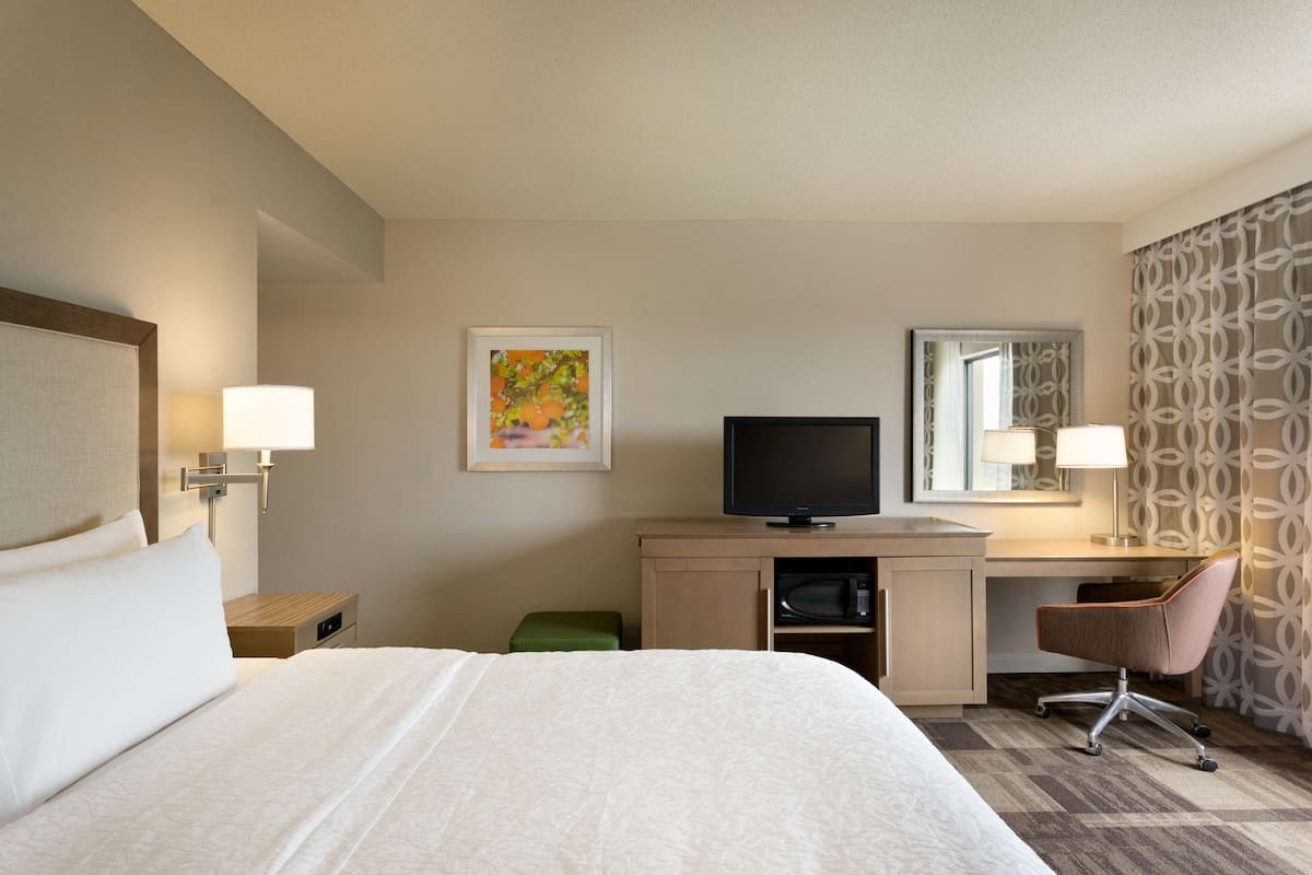 A hotel room with a bed, a desk with a computer, a TV, and a green stool.
