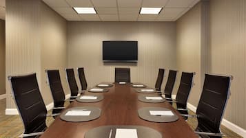Un salón de conferencias con una larga mesa, sillas negras, un televisor de pantalla plana y suelo alfombrado.