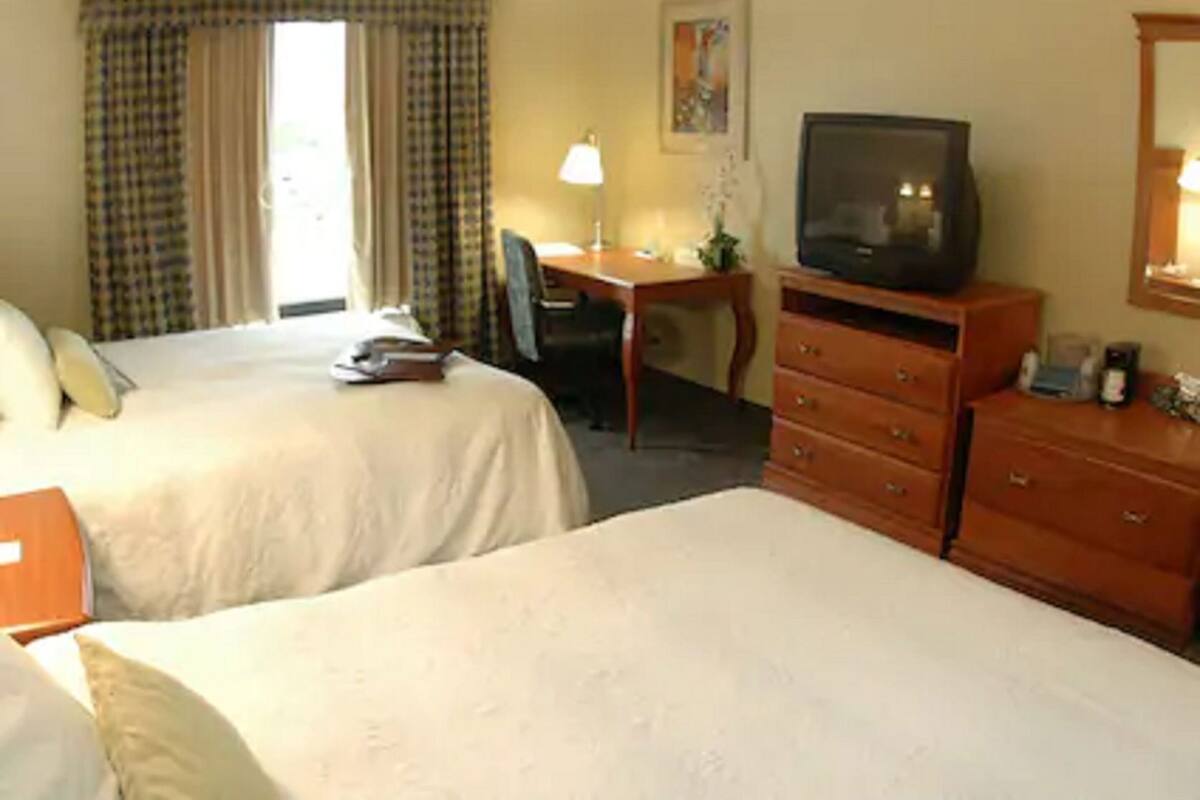 A hotel room with two beds, a desk, a television, and a dresser.